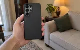 A phone in a plain black case, held in a hand
